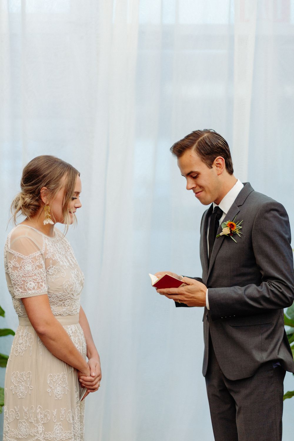 Reading of vows during a wedding ceremony in front of sheer white curtains.