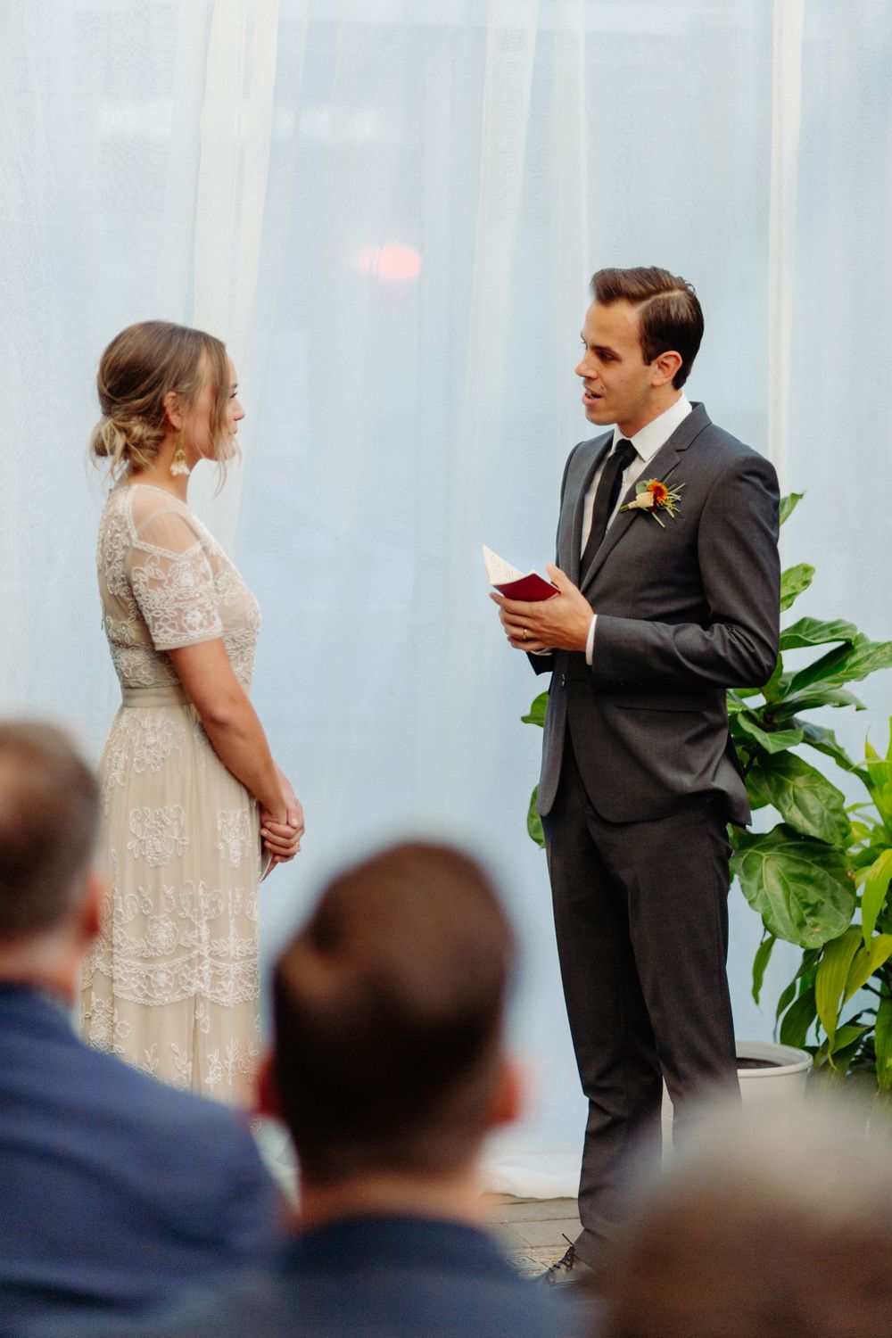 Wedding ceremony in front of white backdrop with guests watching from audience.