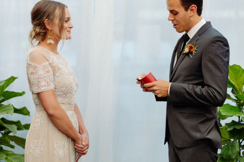 Wedding ceremony moment with bride in lace dress and groom holding red book.