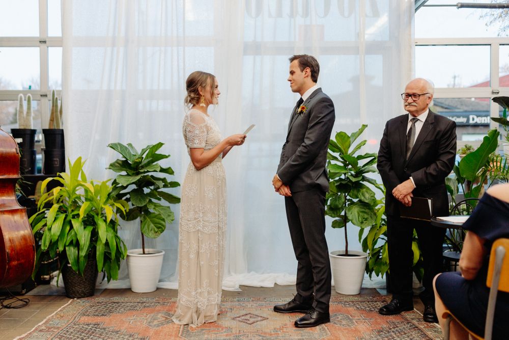 Wedding ceremony with couple and officiant standing in front of white curtain backdrop.
