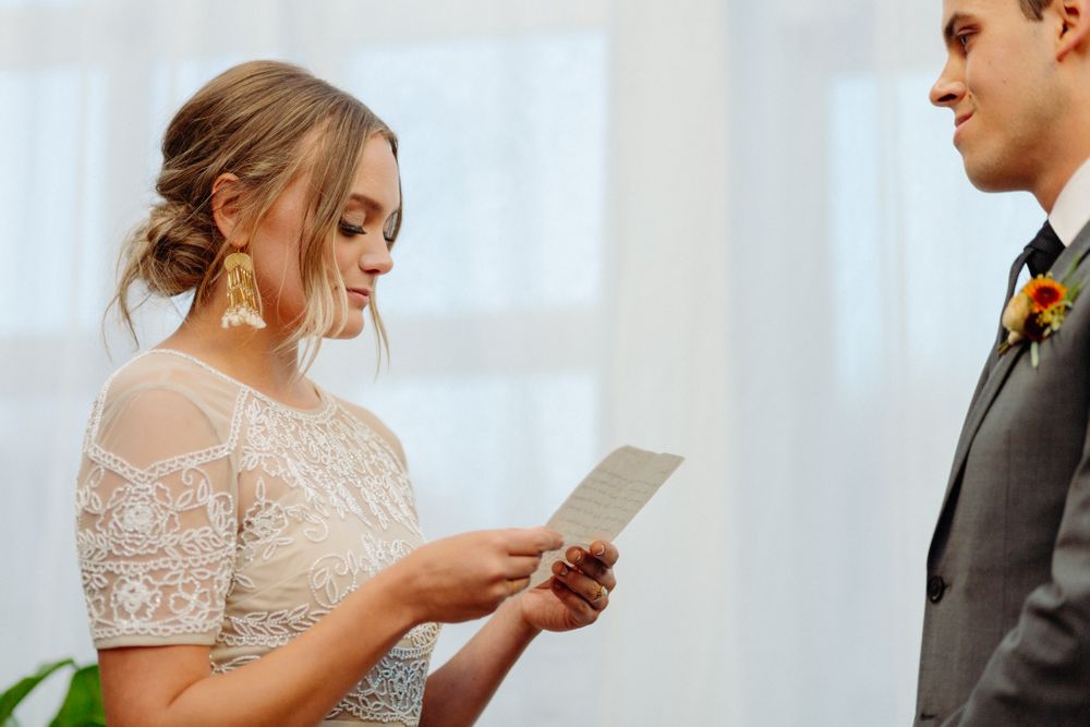 Bride reading from paper during wedding ceremony while groom listens.