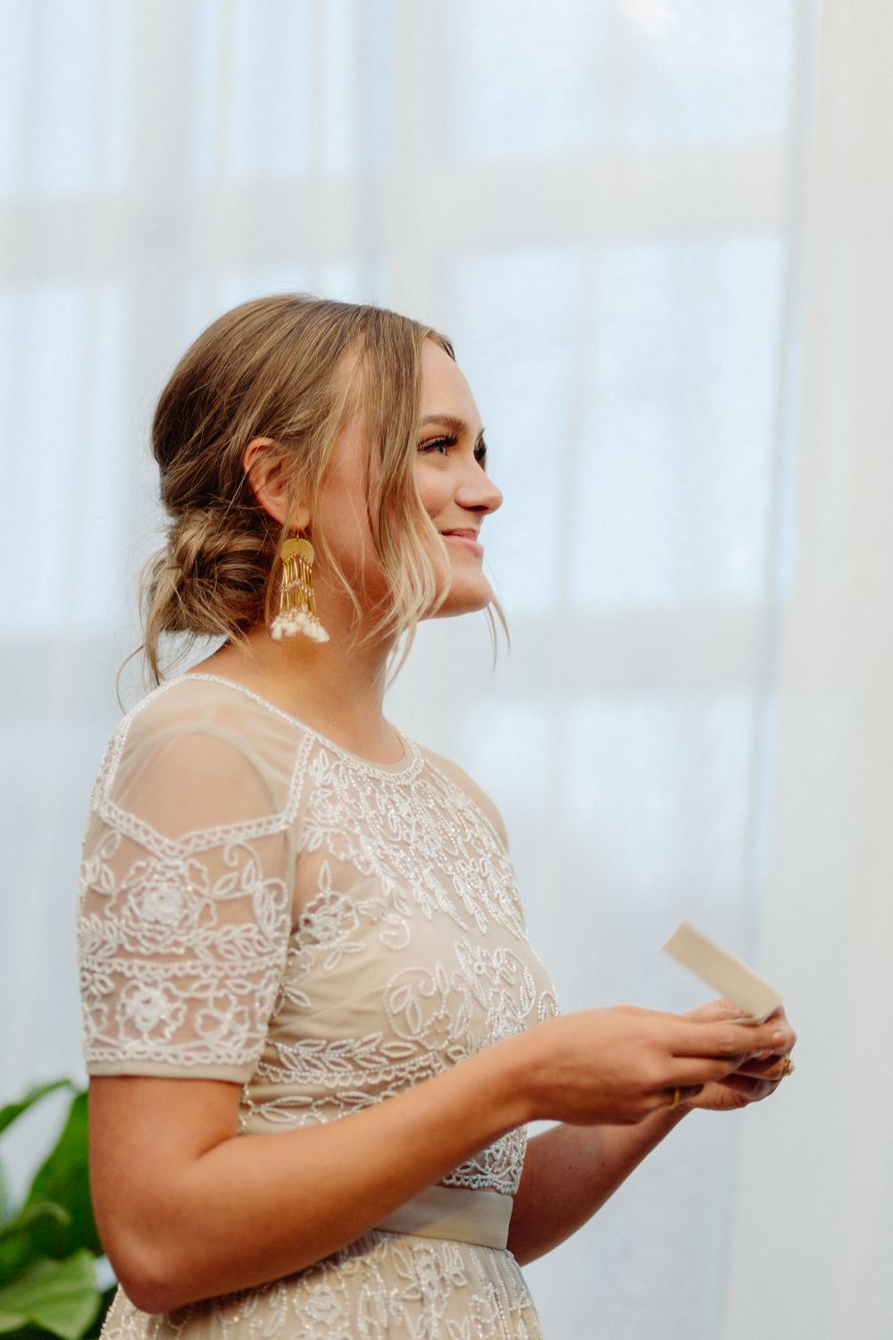 Side profile of bride in lace dress reading during wedding ceremony.