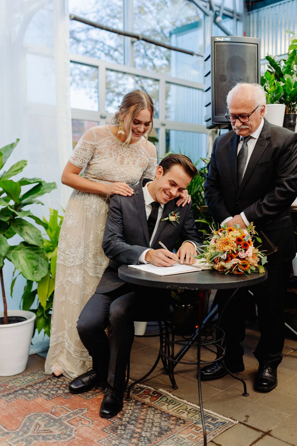Marriage license signing ceremony with couple and officiant at small table.