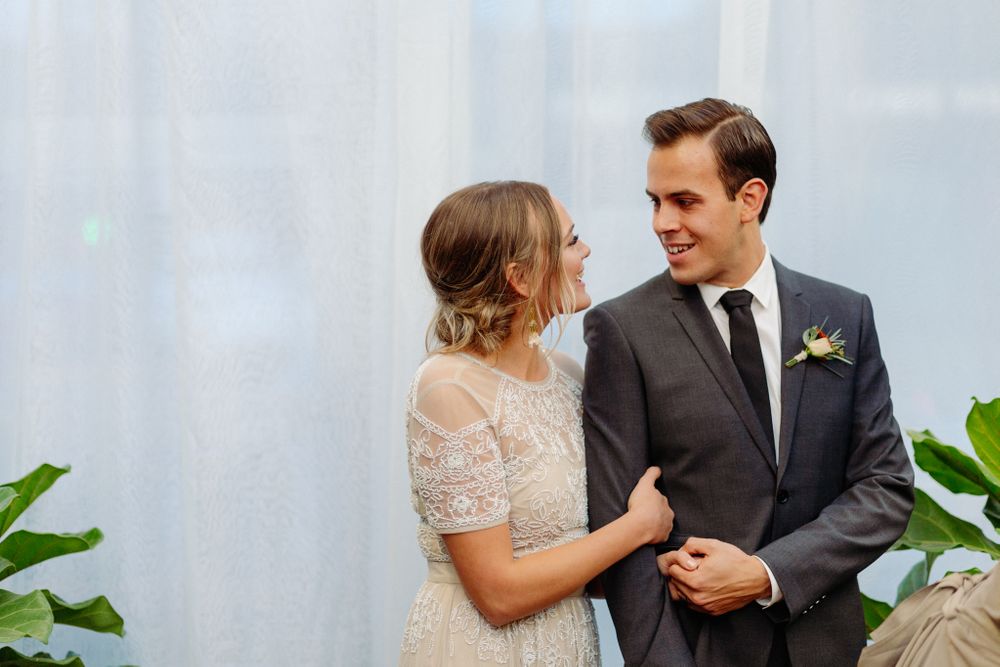 Couple shares intimate moment in front of white curtain backdrop at greenhouse wedding.