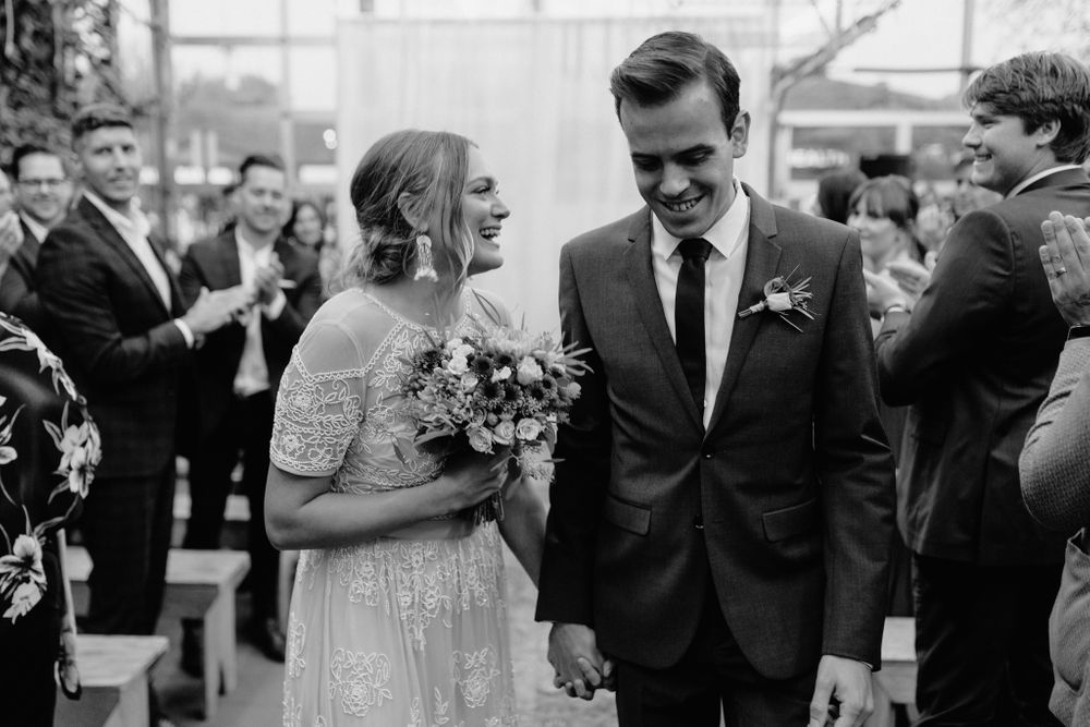 Black and white photo of a wedding couple sharing a happy moment in a greenhouse ceremony space.