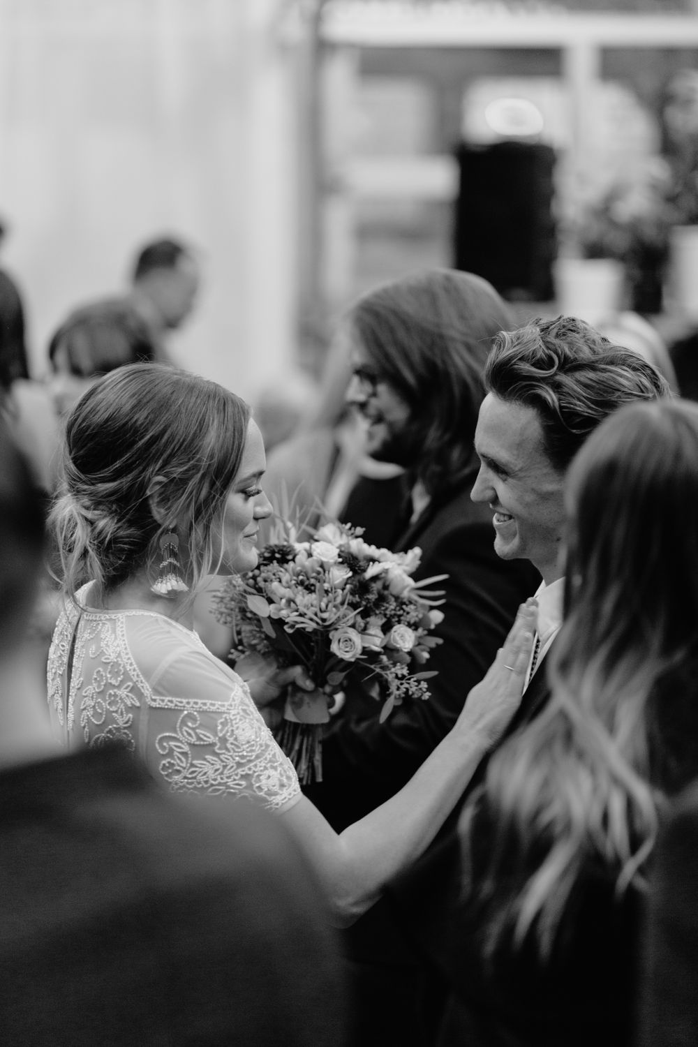 Black and white candid moment of wedding celebration with bouquet in greenhouse setting.