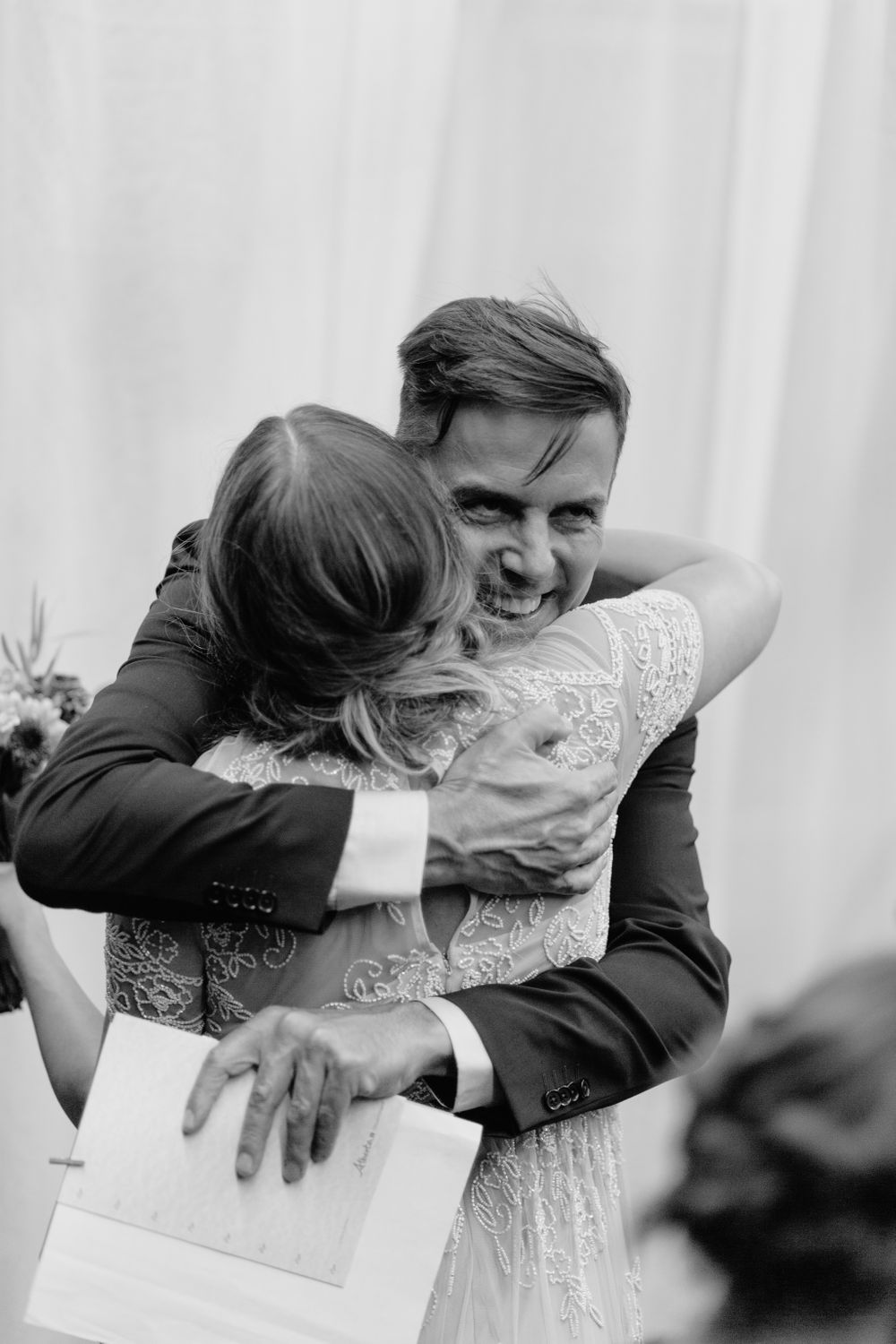 Black and white candid photo of joyful embrace during wedding ceremony.