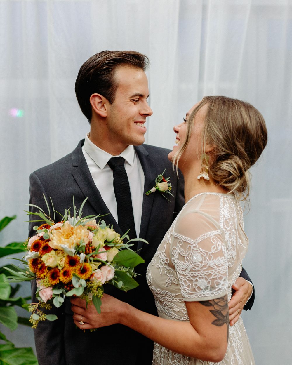 Couple shares intimate moment with autumn bouquet against white backdrop during greenhouse wedding.