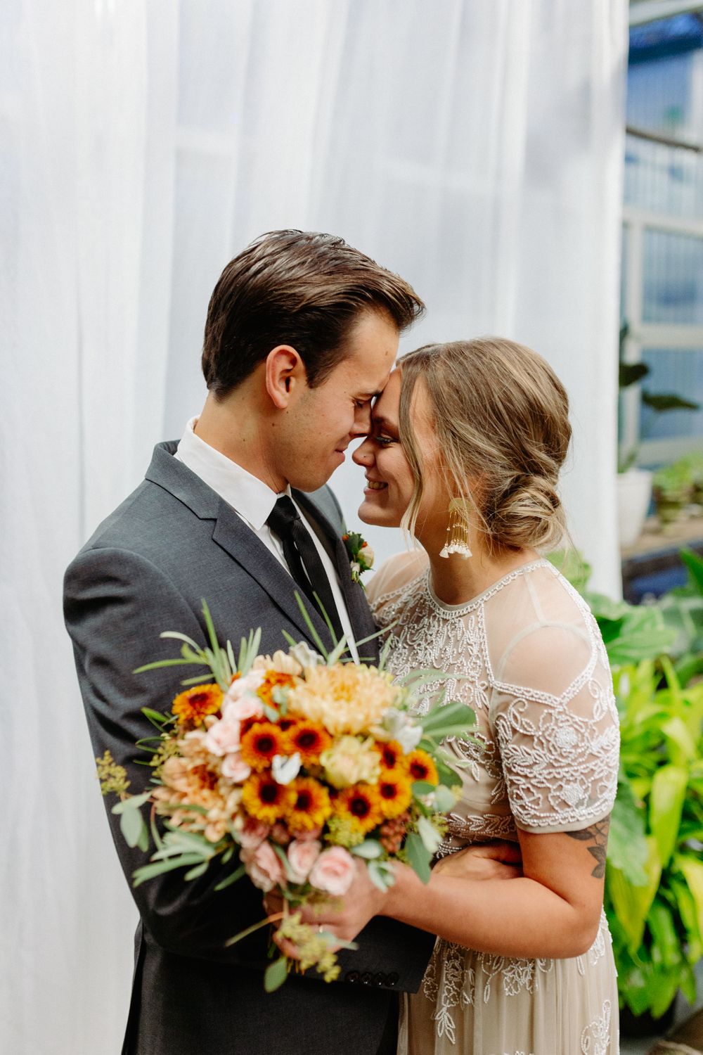 A romantic wedding couple shares an intimate moment with sunflowers and roses in her bouquet.