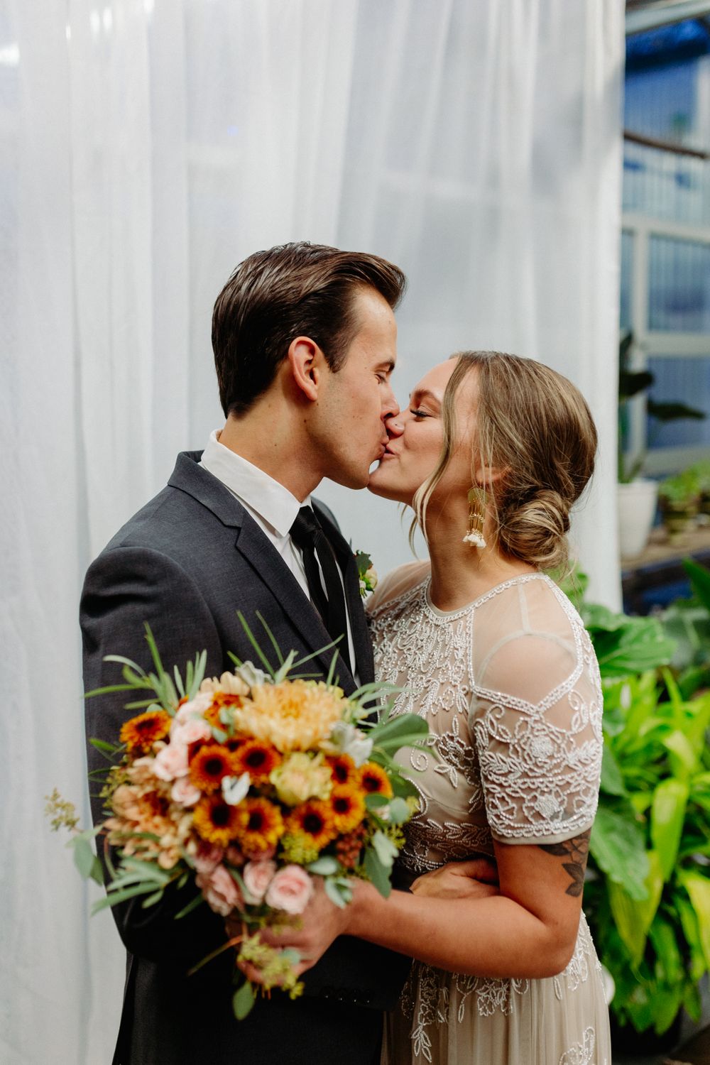A tender wedding kiss moment captured with a colorful autumn bouquet.