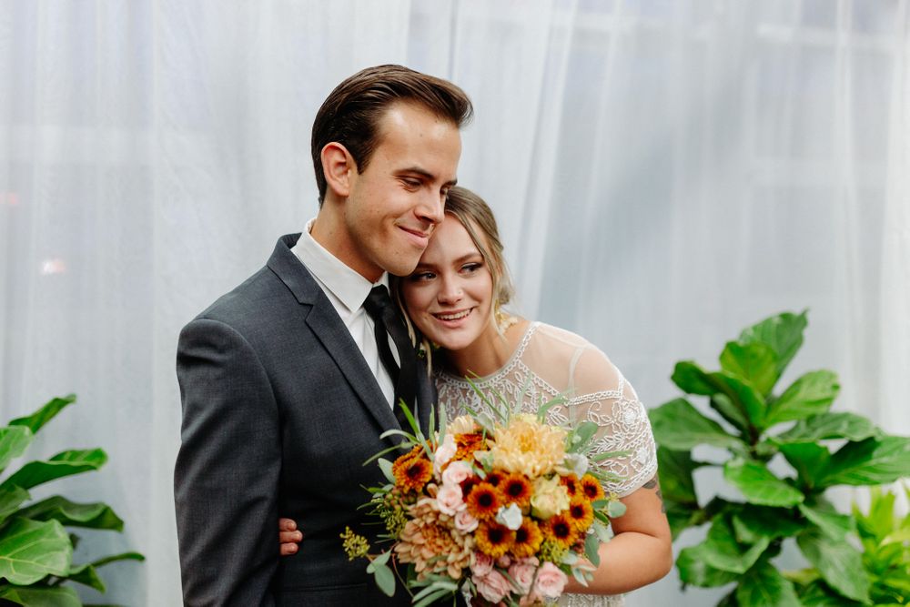 A joyful wedding couple embracing against a white curtain backdrop with greenery.