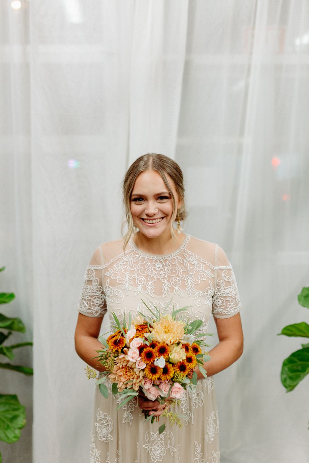 A vintage-inspired lace wedding gown paired with an autumnal bouquet of orange and burgundy flowers.