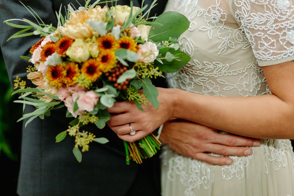 Close-up of bridal bouquet with sunflowers and roses held between bride and groom.