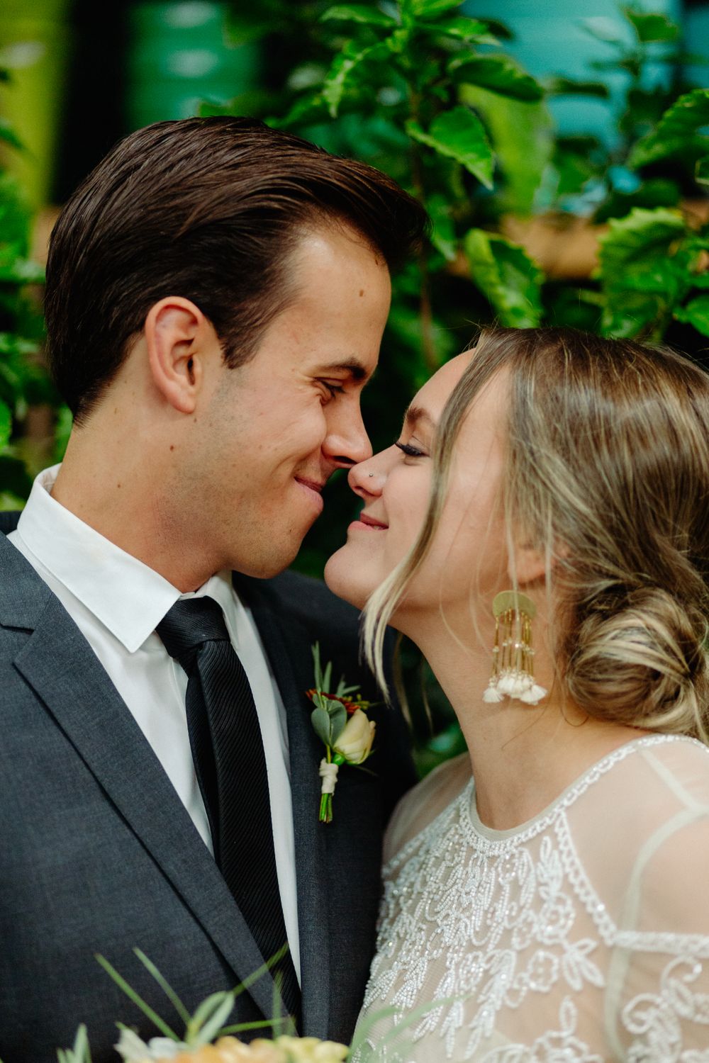 Intimate moment between newlyweds surrounded by green foliage.