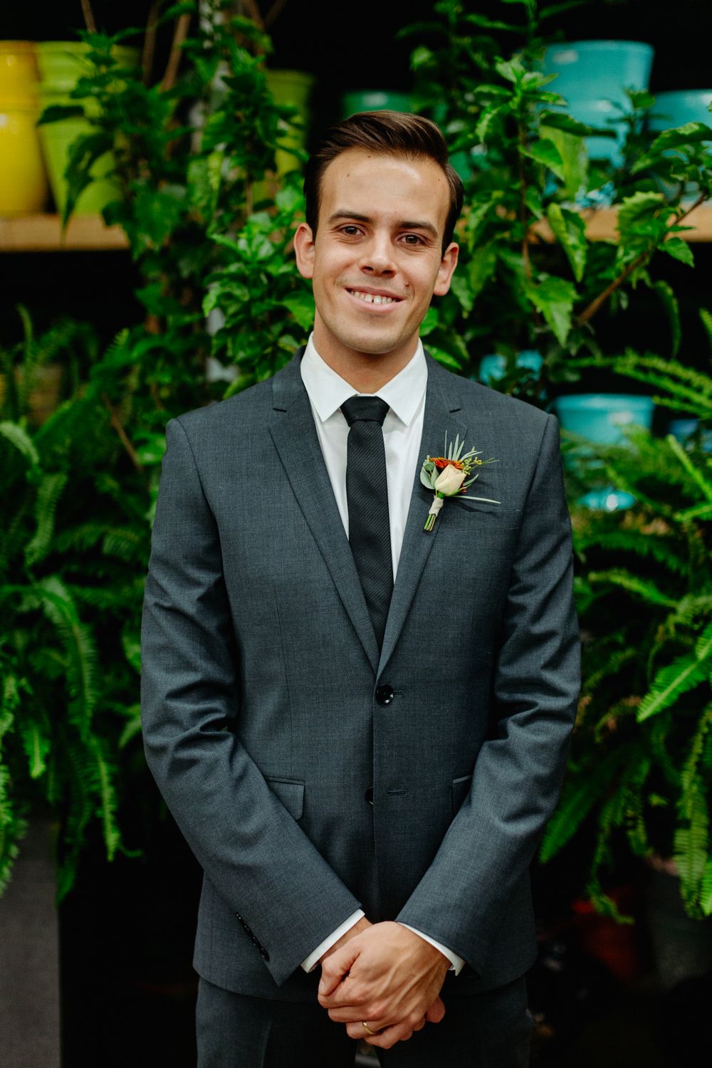 Groom in grey suit with boutonniere smiles against garden background.
