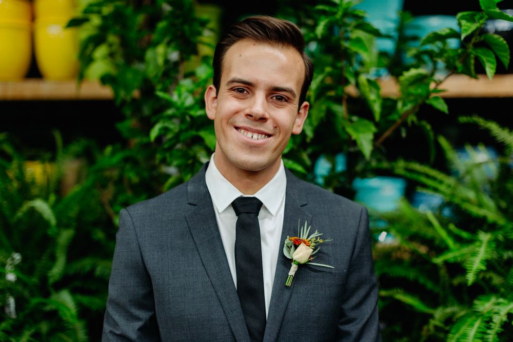 Portrait of groom wearing charcoal suit against colorful garden display.