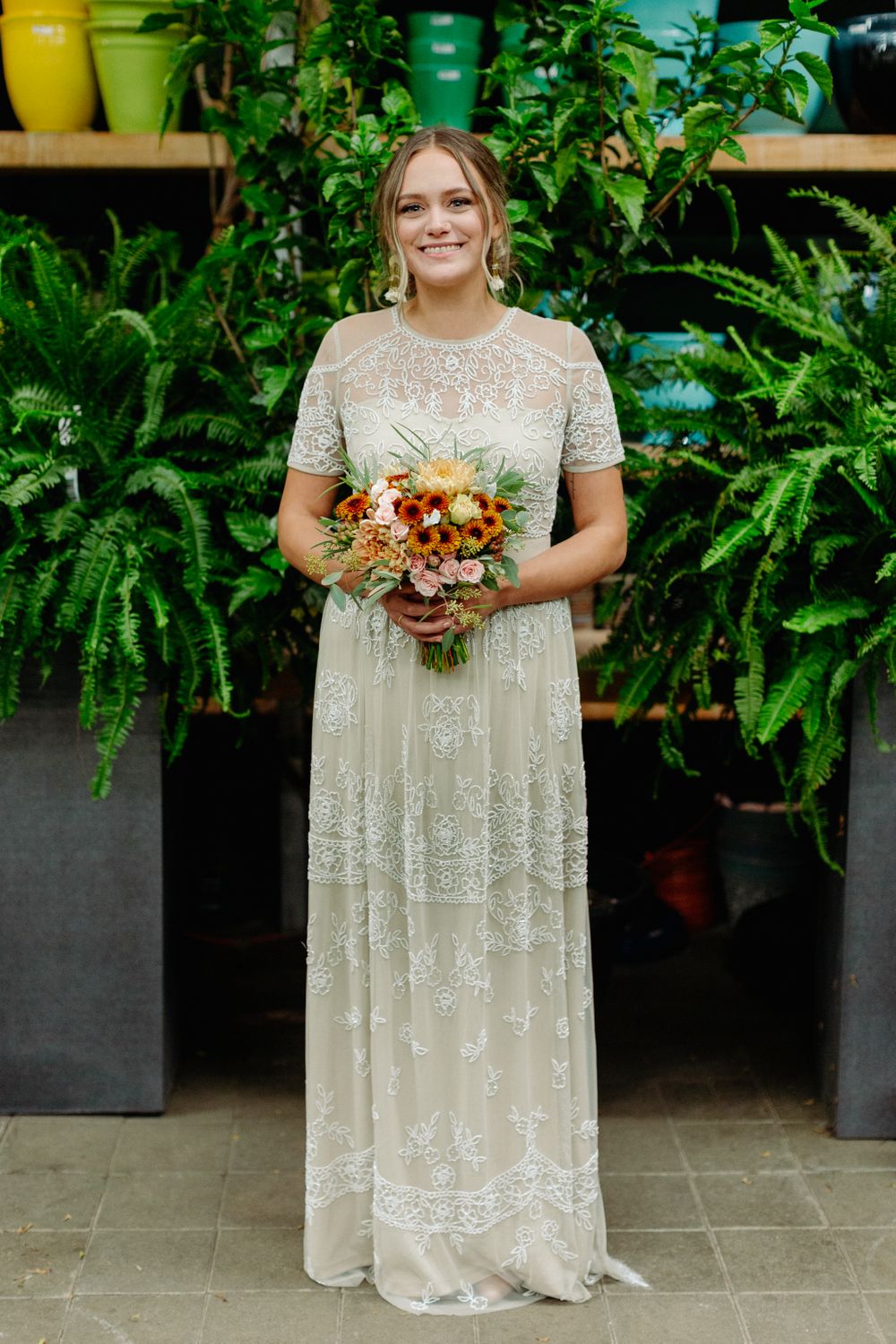 Full-length portrait of bride in vintage-inspired lace gown with fall bouquet.