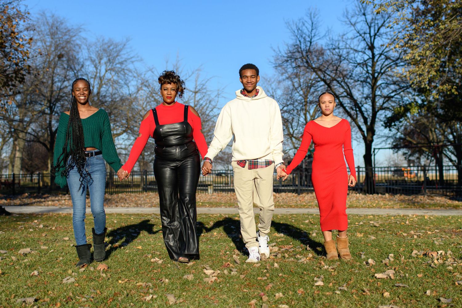 Four friends standing together in casual poses on fallen autumn leaves in a park.