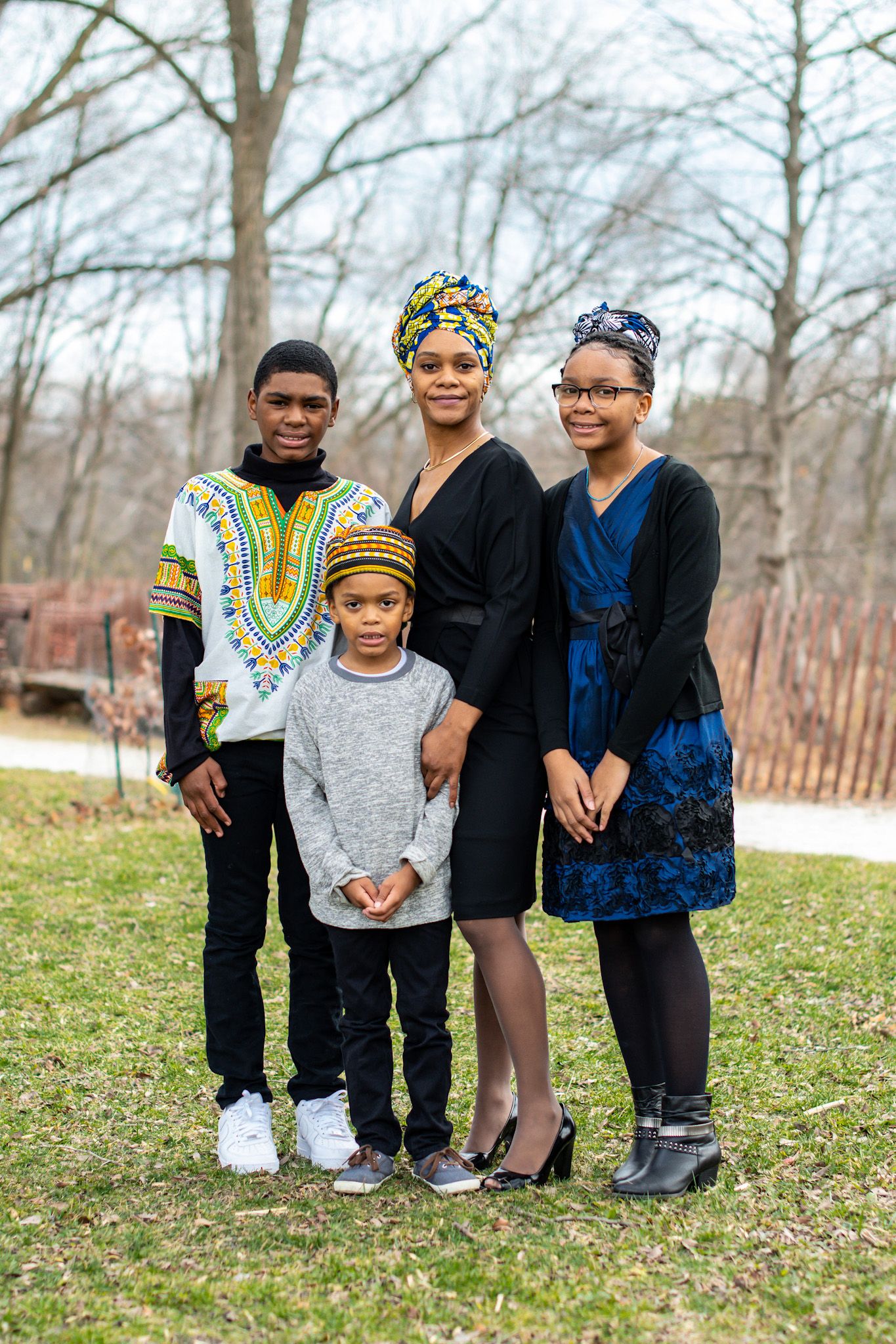 Family group wearing mix of casual and traditional clothes poses together outdoors on grassy lawn.