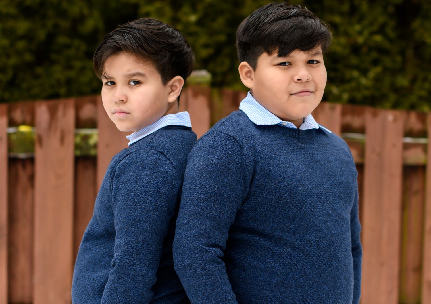 Two youth in matching navy sweaters pose back-to-back outdoors.