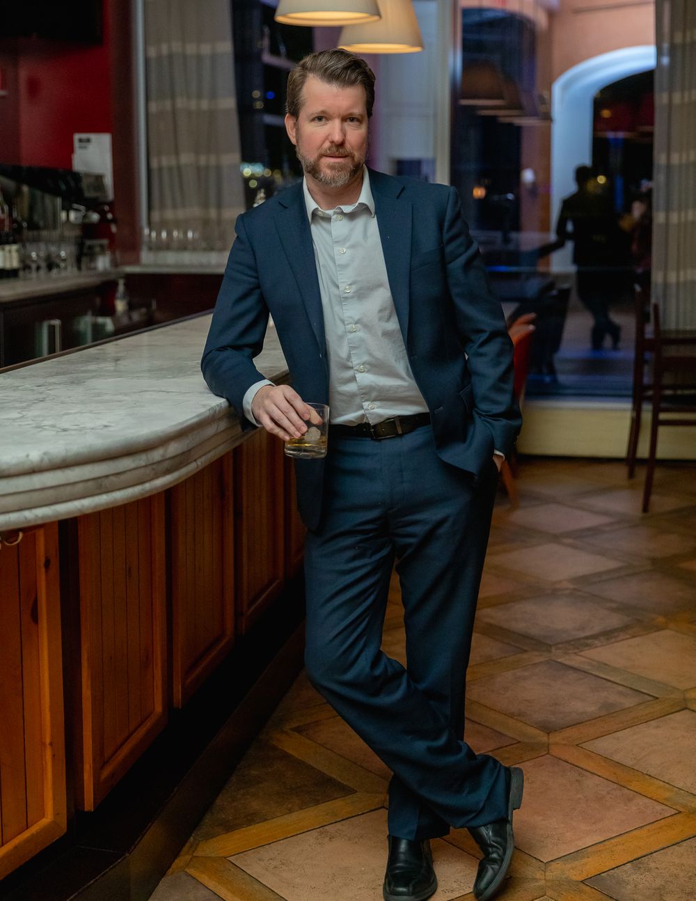Business professional in dark suit relaxing at upscale bar with wooden interior.