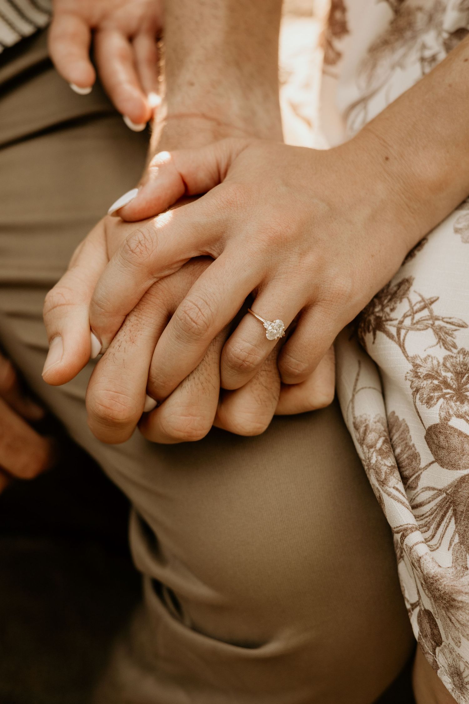 Hands with diamond ring against floral patterned fabric in sepia tones.