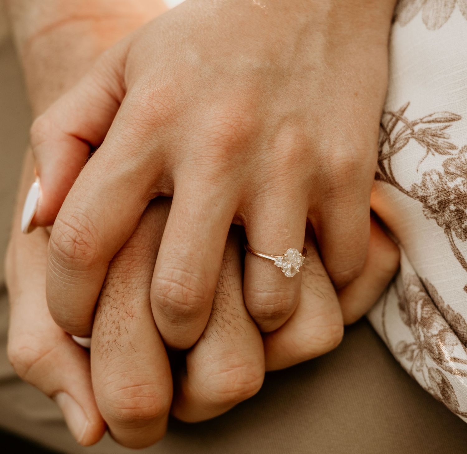 Close-up of hands with engagement ring resting on a neutral surface.