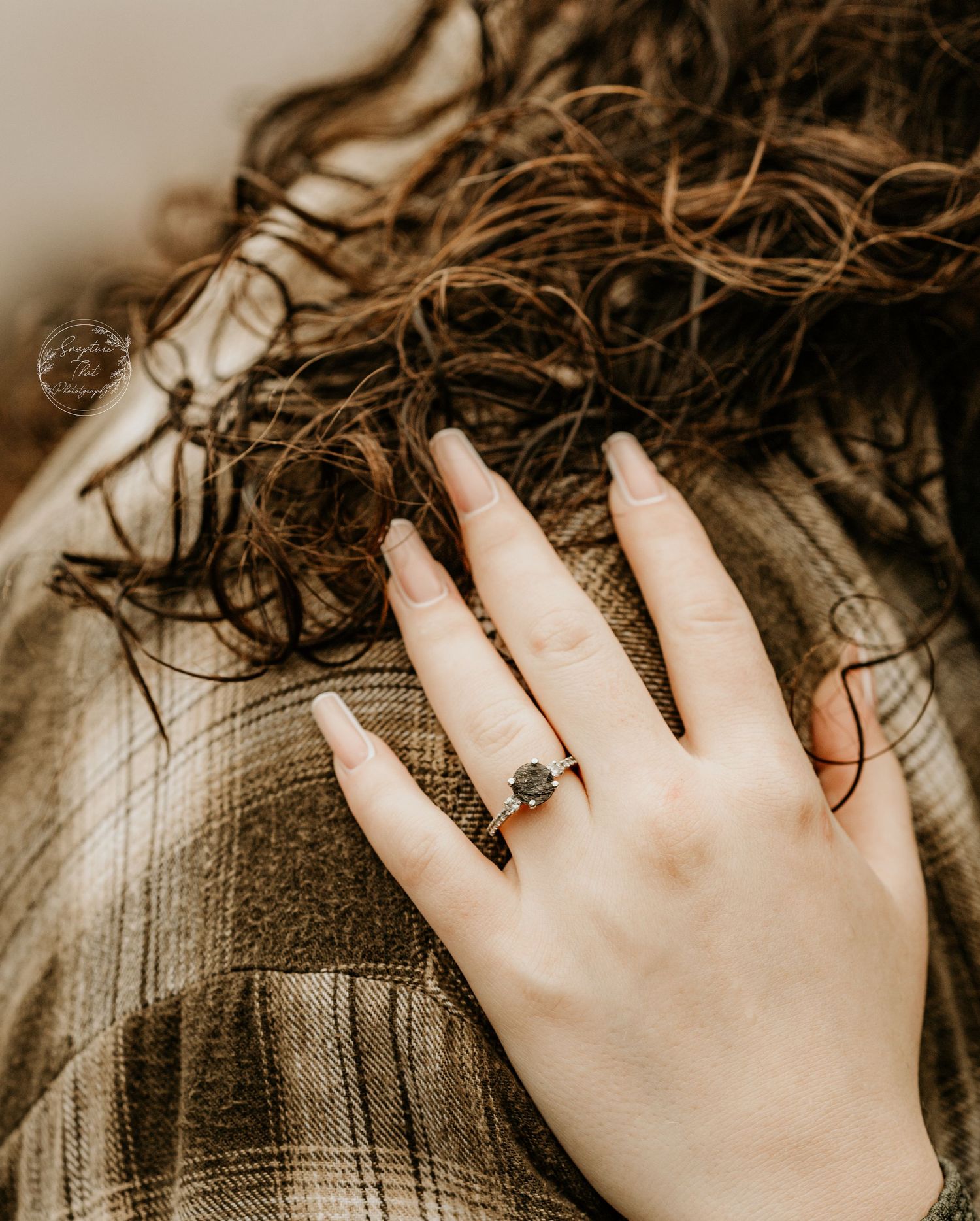 Hand with engagement ring resting on textured plaid fabric in sepia tones.