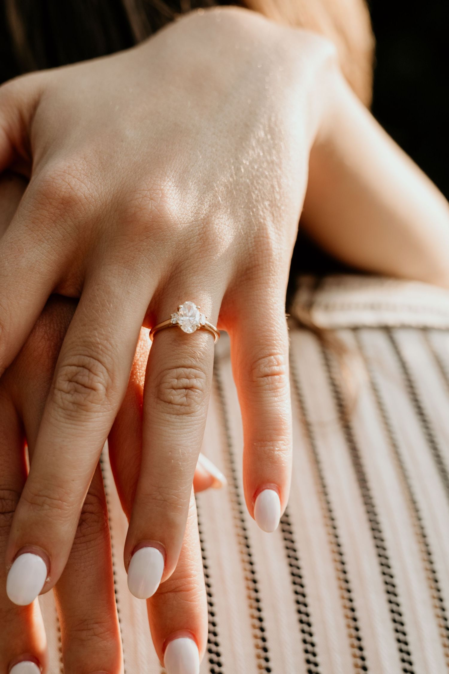 Close-up of hands with white manicured nails and diamond engagement ring on finger.