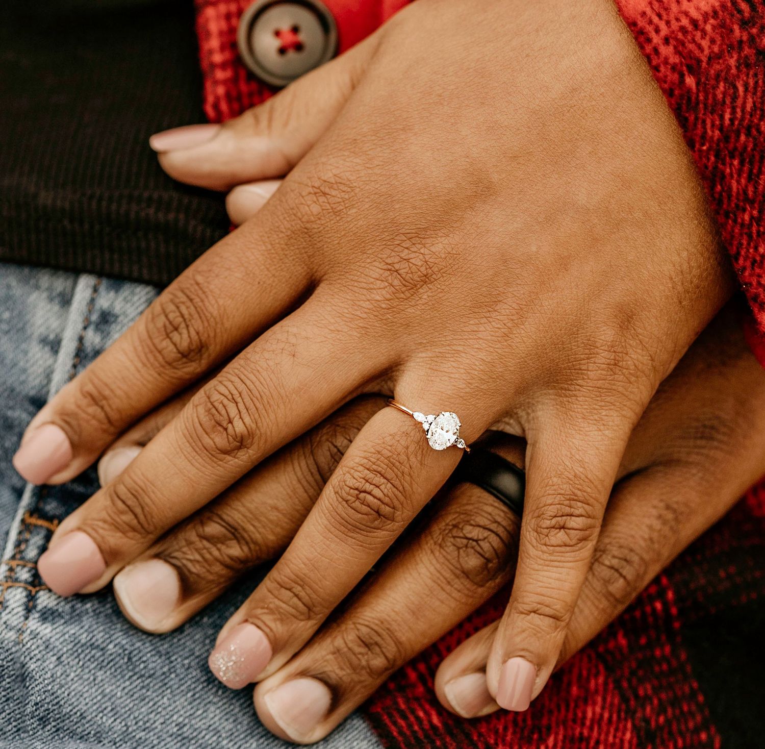 Close-up of hands with an engagement ring against denim and red fabric textures.