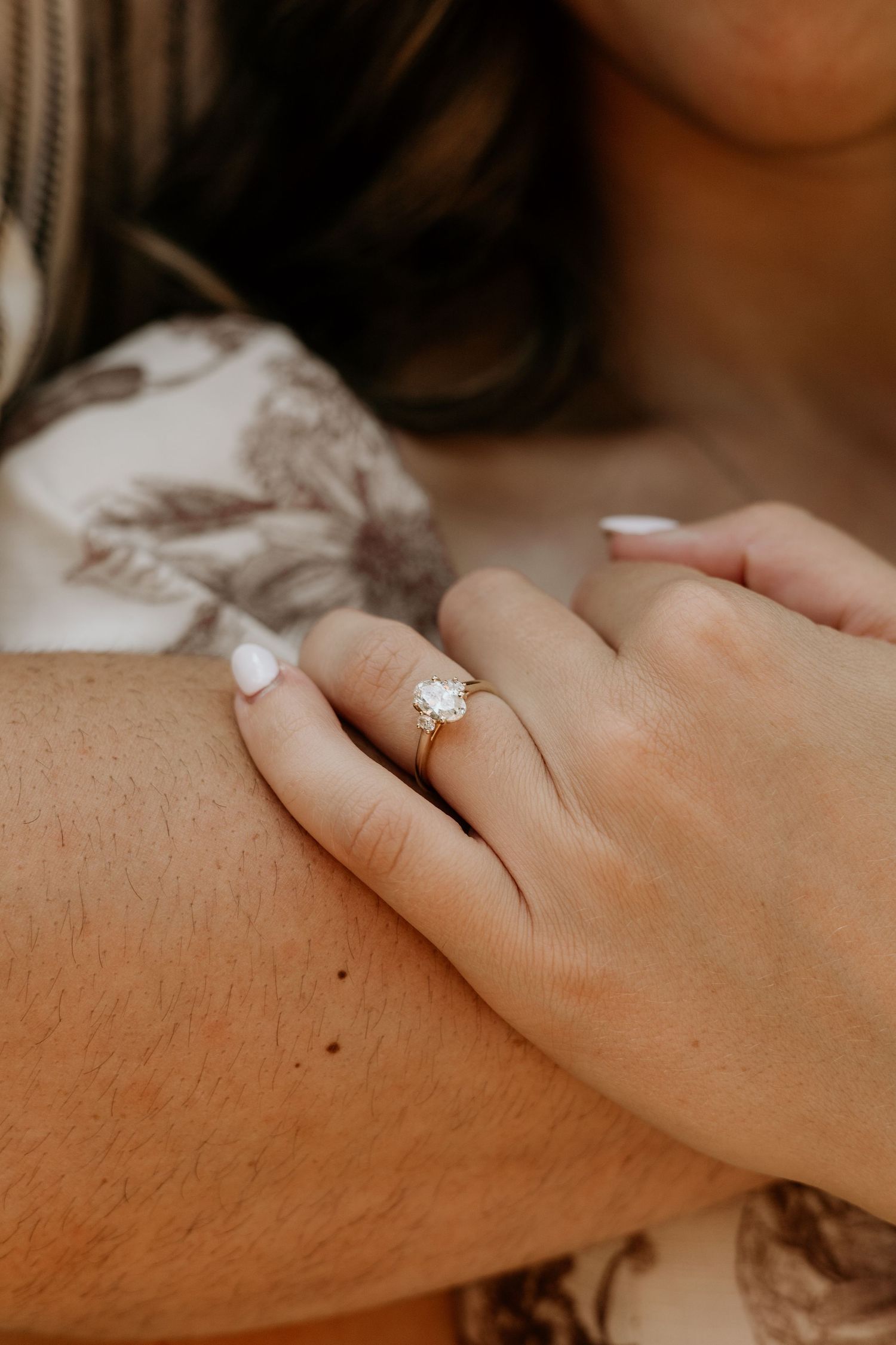 Diamond engagement ring sparkles on hand against warm neutral background.
