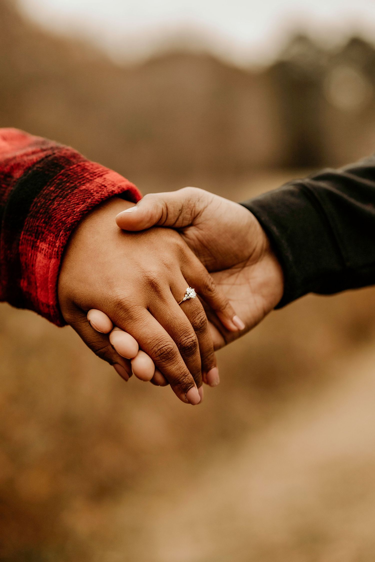 Two hands clasped together with one wearing a red sleeve, captured in warm sepia tones.