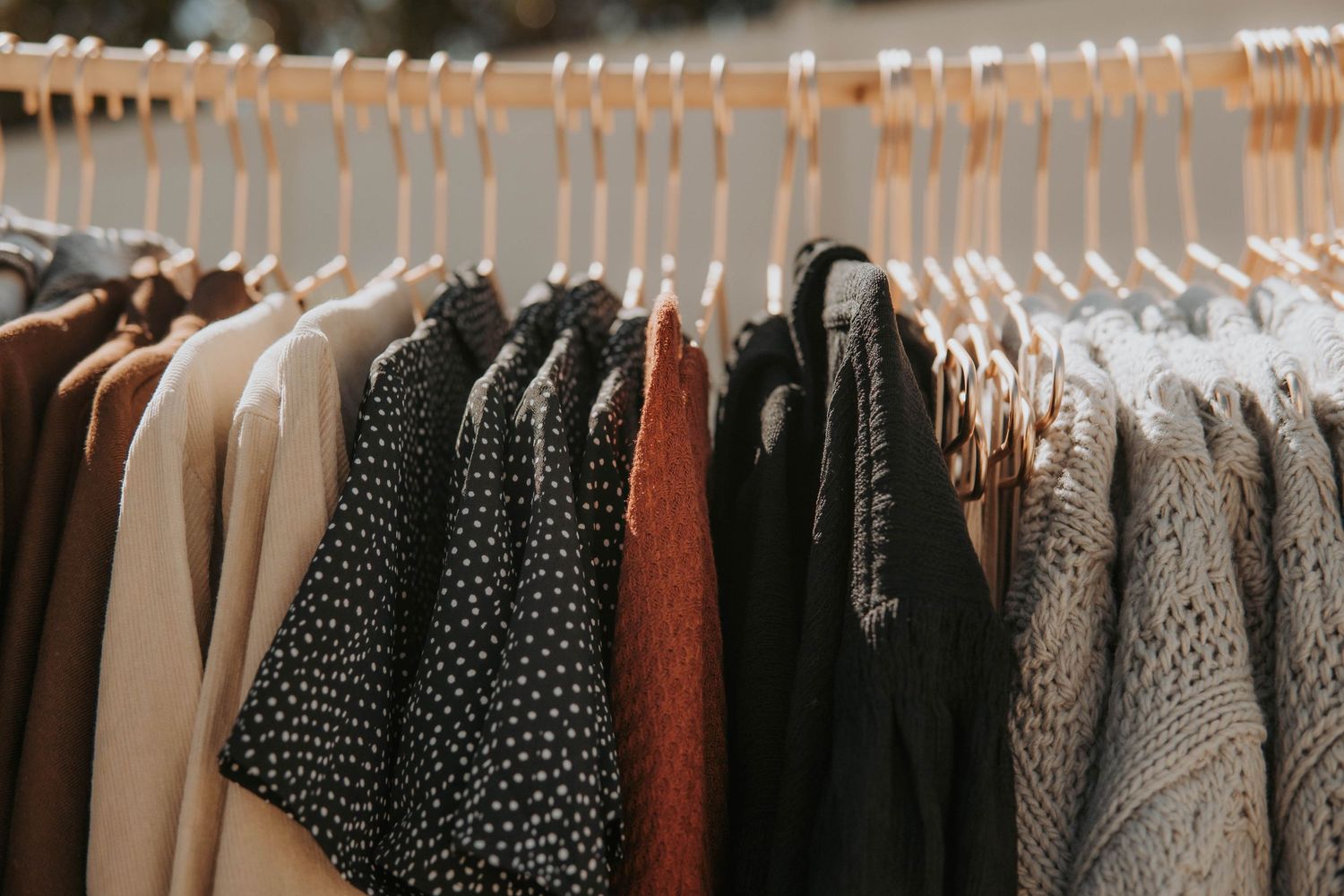 A rack of clothing featuring polka dot patterns and neutral tones hangs neatly on hangers.