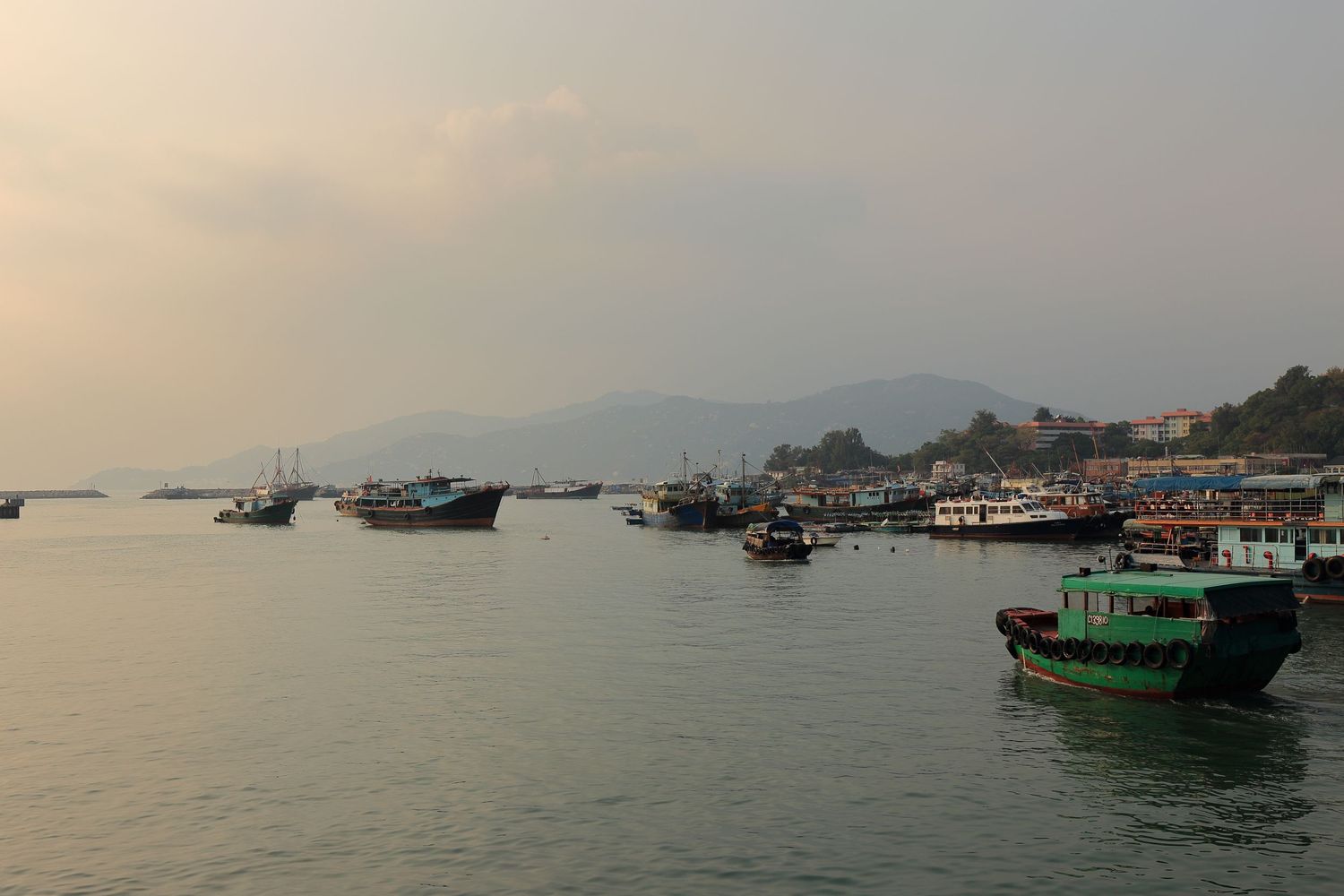 Fishing boats and vessels anchored in misty harbor during sunset.