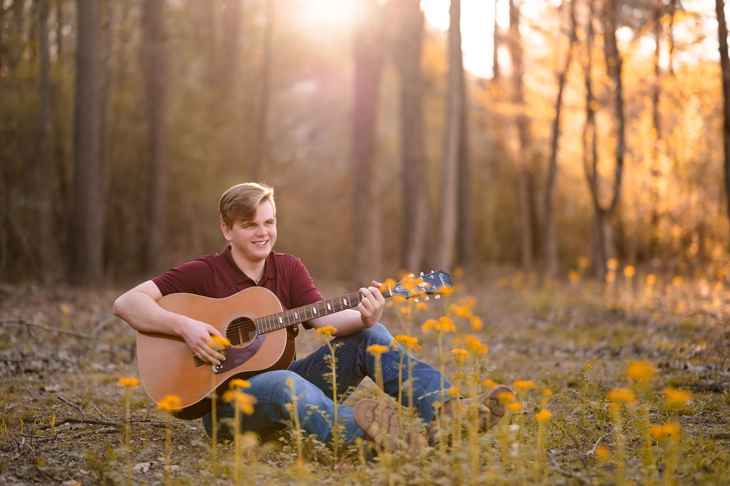 Musician playing acoustic guitar in sunlit forest during golden hour.