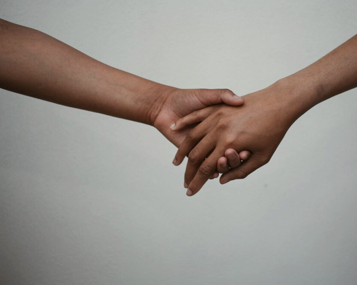 Two black hands reach for each other and hold their other person’s hand