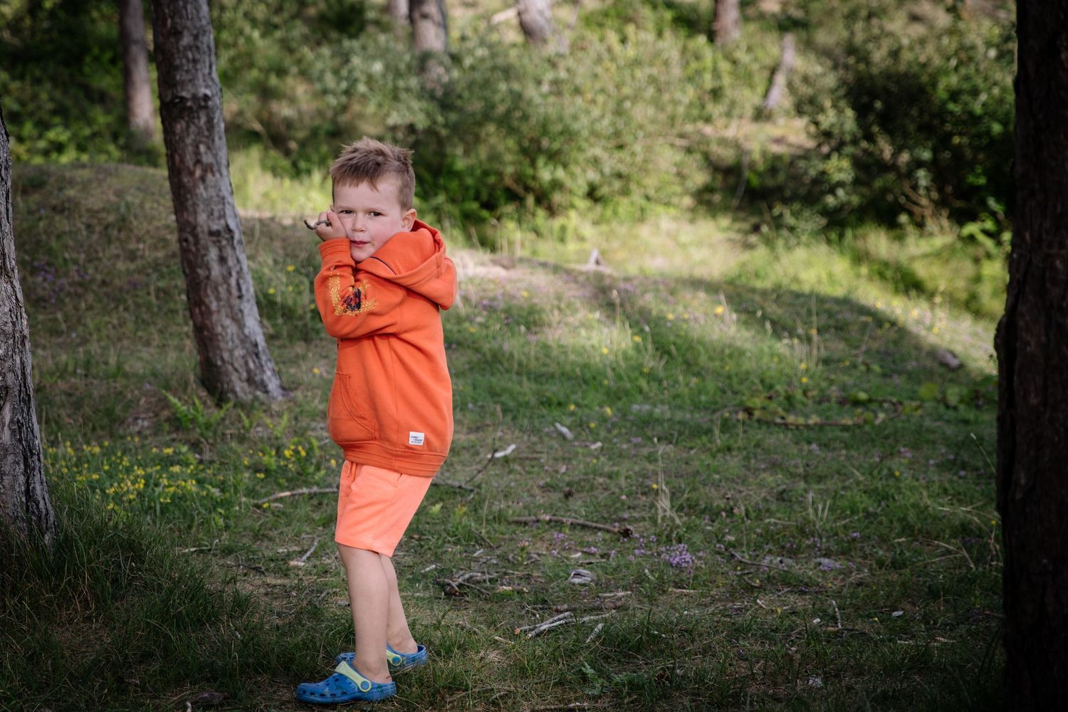 Child in bright orange clothing playing outdoors among trees.