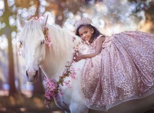 Dreamy portrait featuring a white horse adorned with pink flowers and a sparkly pink princess dress in a magical forest setting.