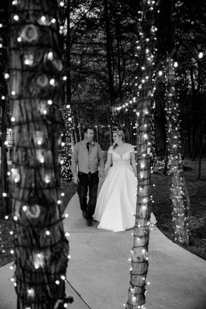 Black and white photo of couple walking along path lit with twinkling fairy lights.