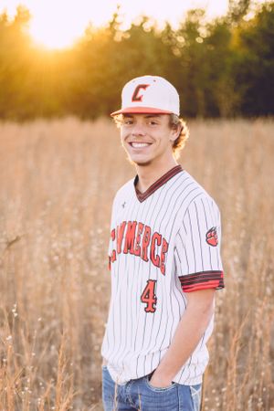 Baseball player in white pinstripe uniform poses in golden field at sunset.