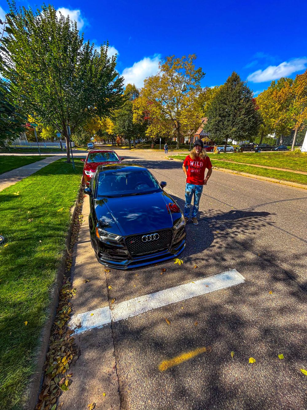 Blue Audi sports car parked on a tree-lined street during autumn with golden foliage.