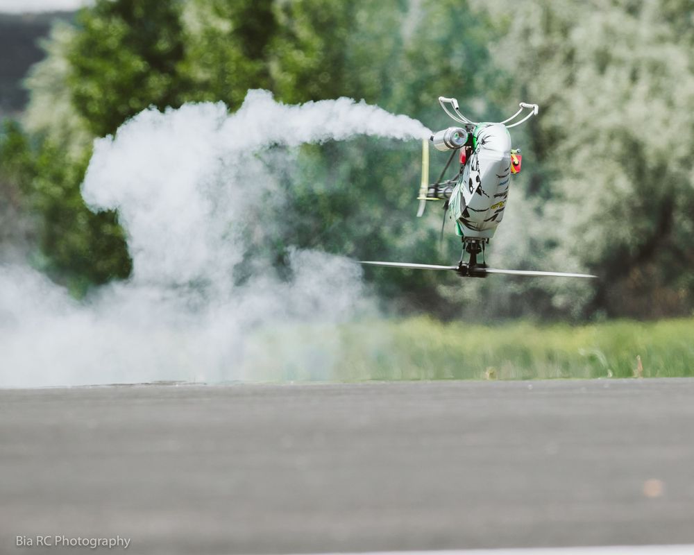 Remote controlled helicopter performing stunt through smoke cloud on outdoor track.