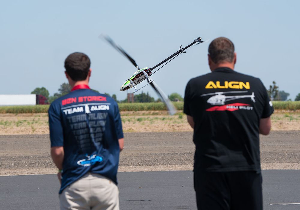 Two RC helicopter pilots operating their crafts during an outdoor demonstration.