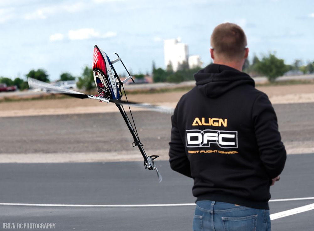 RC helicopter pilot wearing Align DFC hoodie controlling aircraft on flying field.