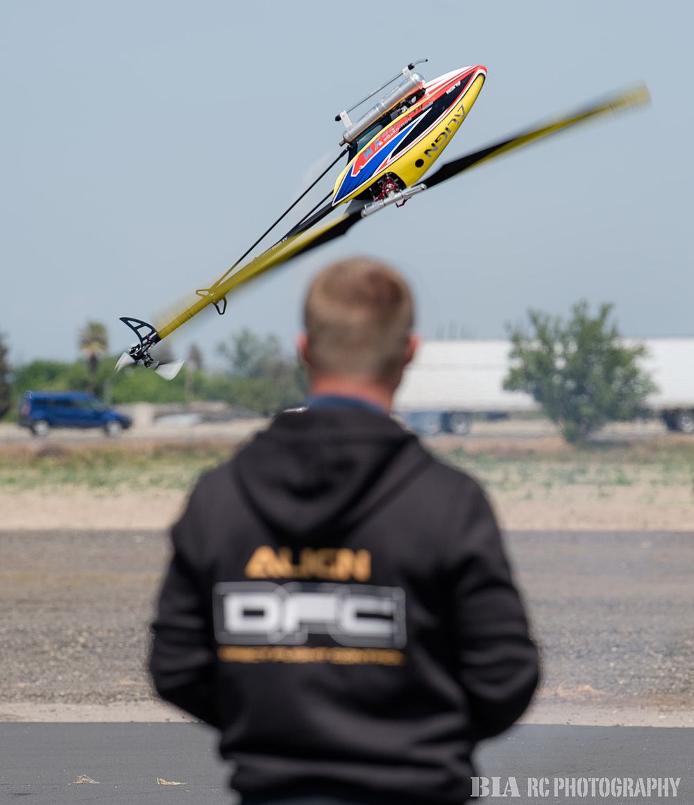 RC helicopter pilot in Align DFC hoodie controlling colorful helicopter in flight.