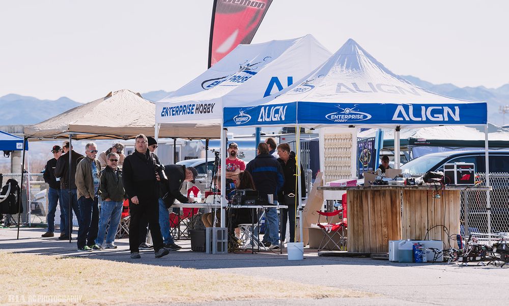 Outdoor RC event setup with multiple vendor tents and attendees gathered under Align banner in desert setting.