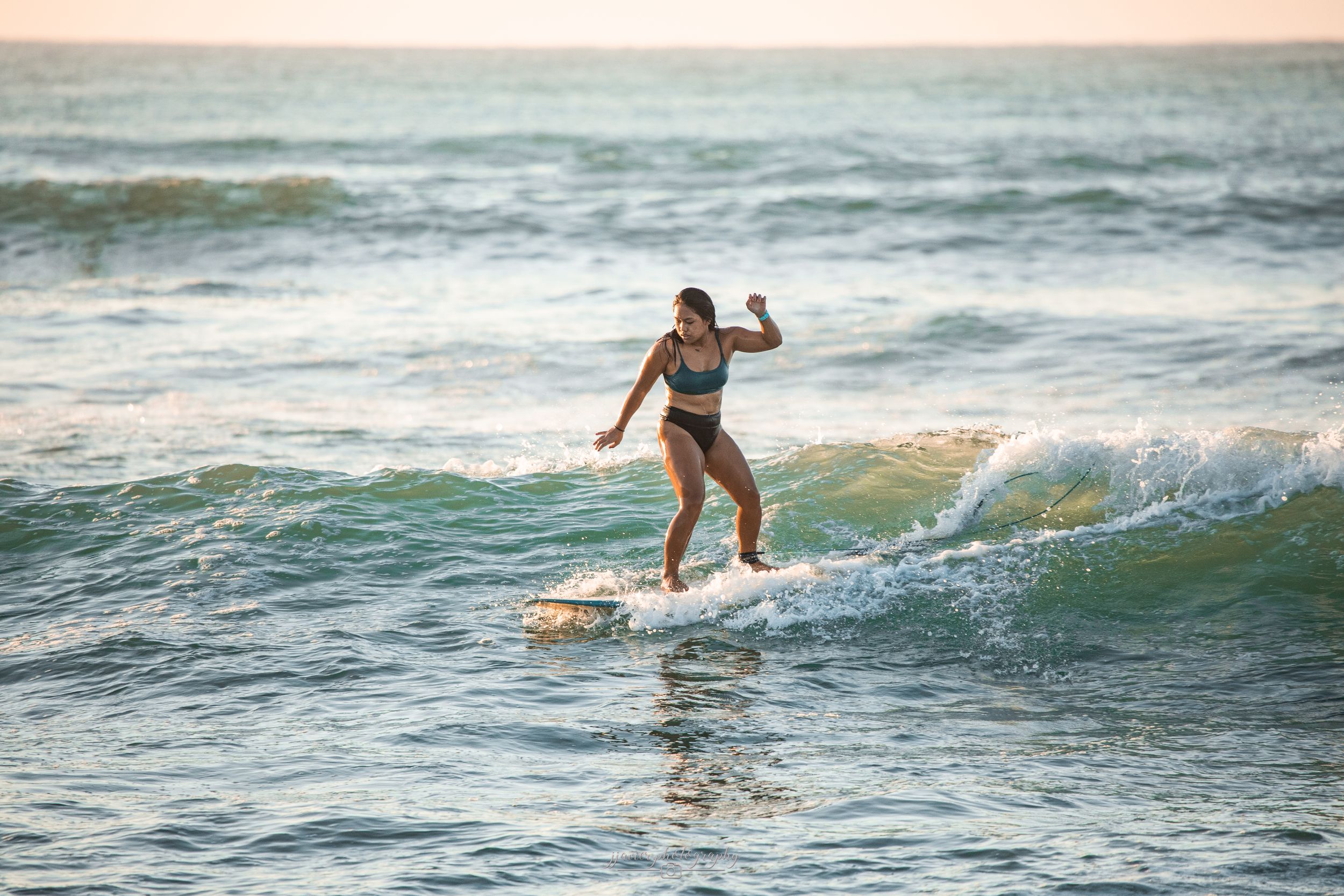 Surfer glides along wave during sunset with golden light reflecting on water.