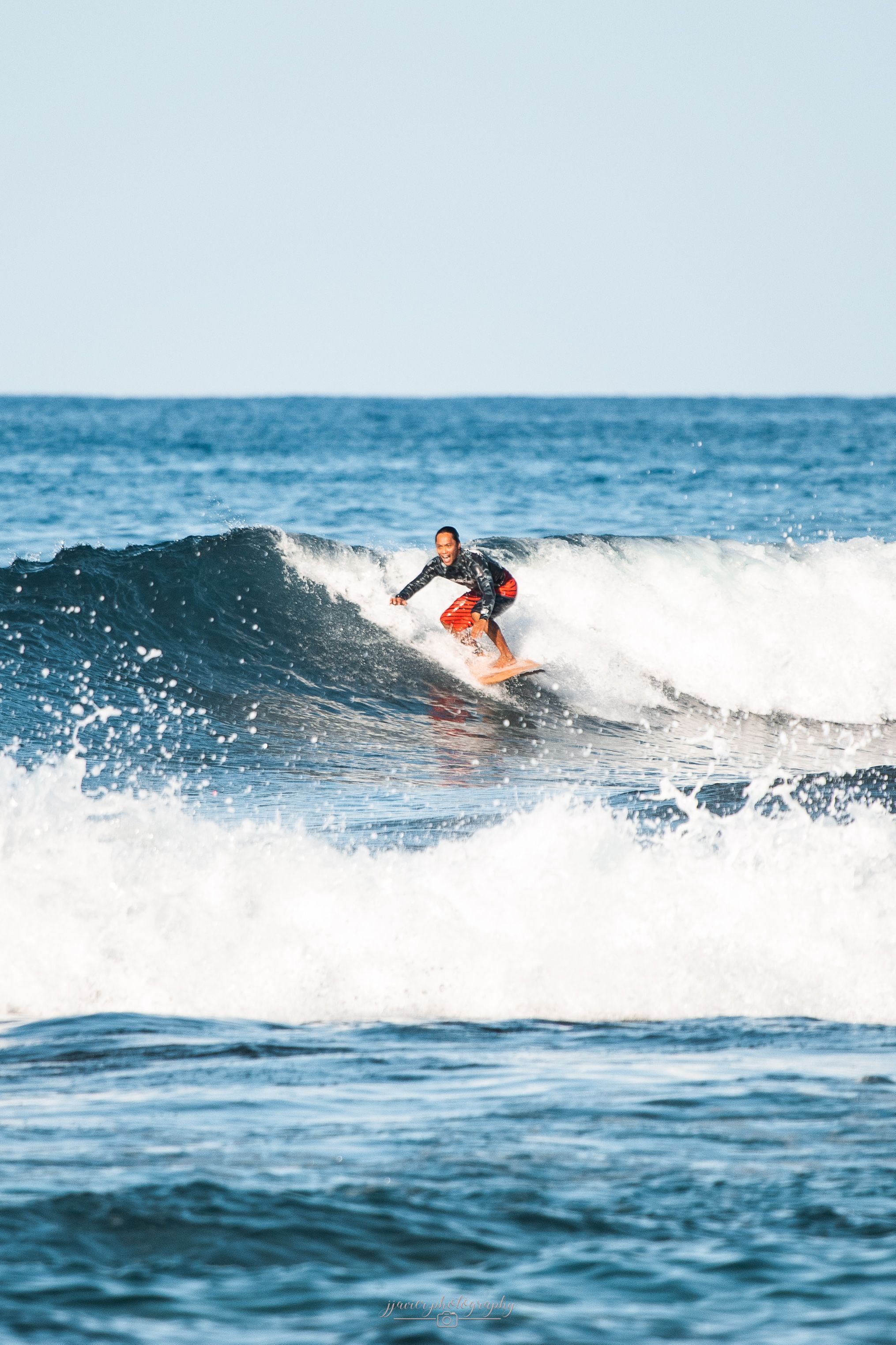 Surfer rides ocean waves on a bright sunny day with white water spray.