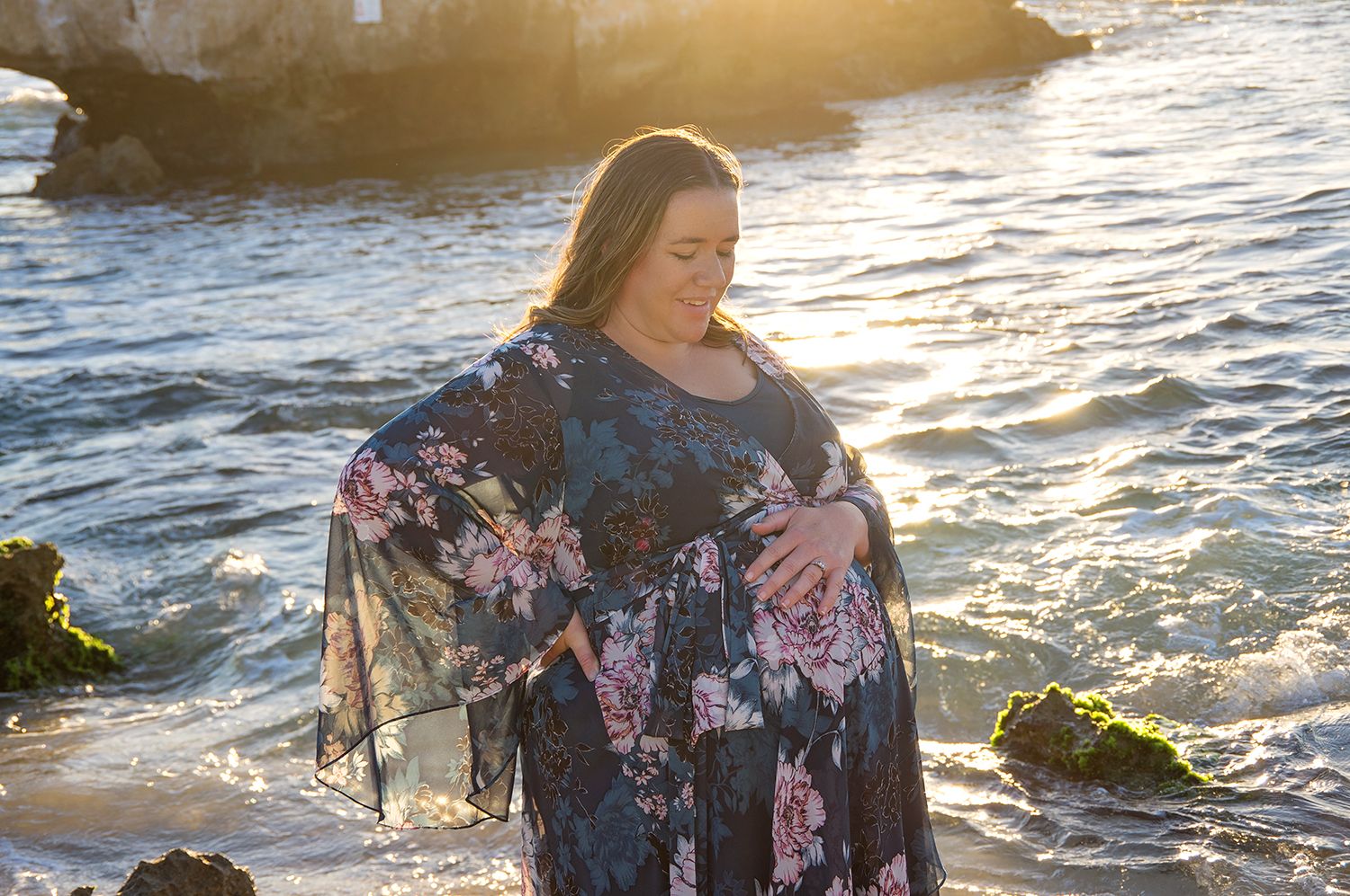 woman on beach touching pregnant belly