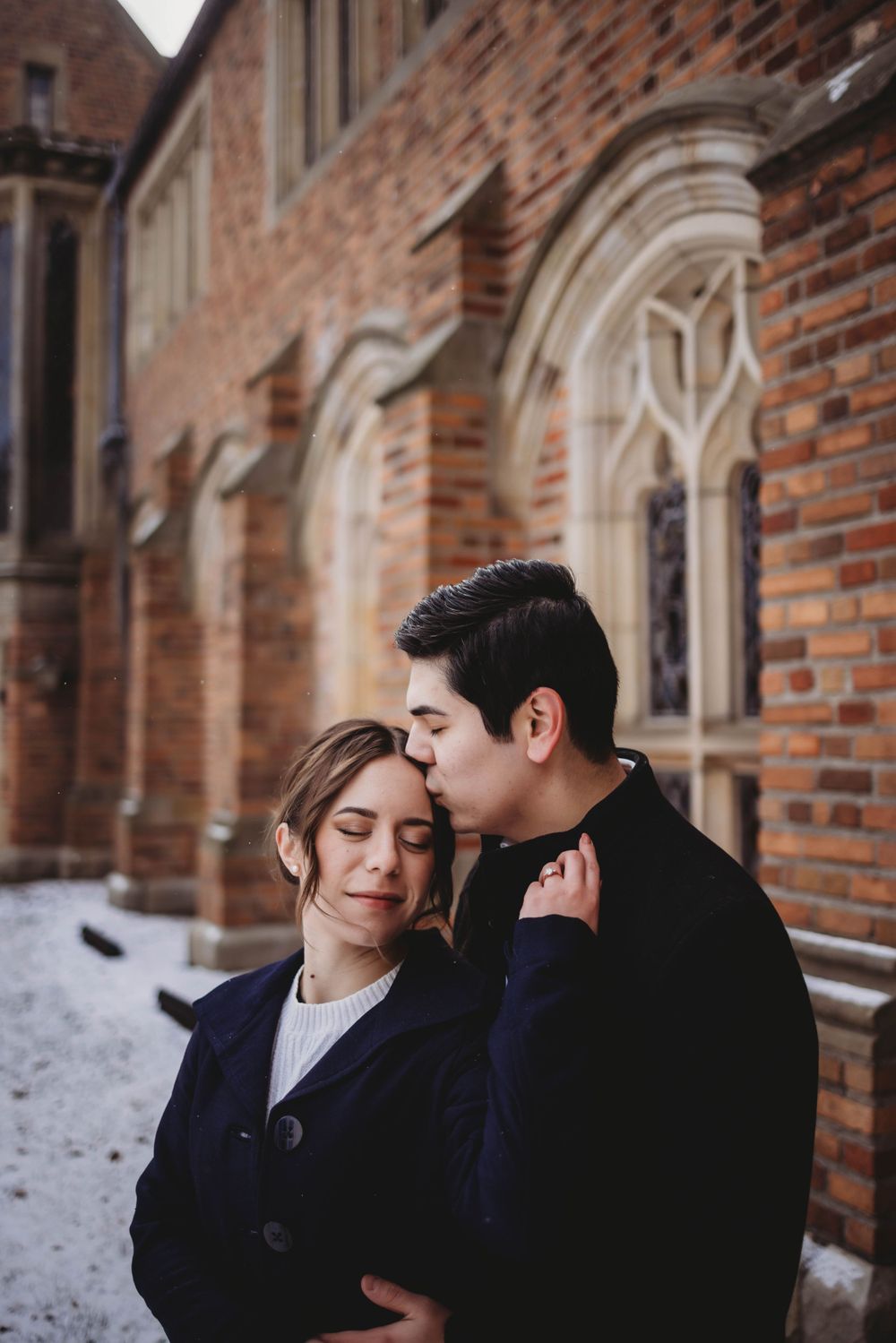 A tender moment against a historic brick building with gothic architecture in winter.